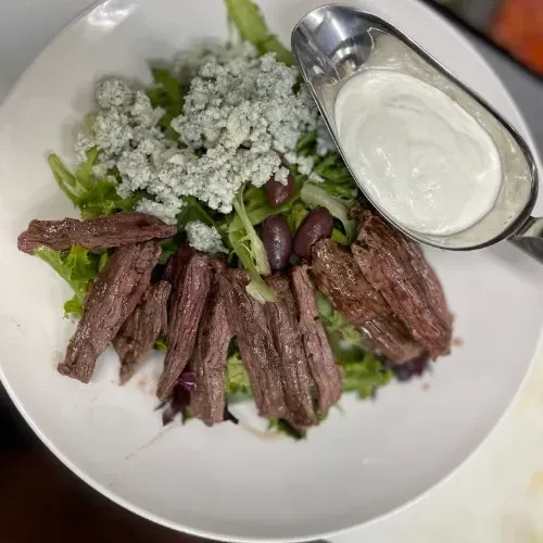Steak salad with blue cheese, olives, and a side of dressing.