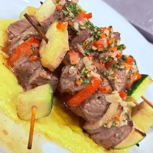 Skewers of meat and vegetables on a yellow purée.