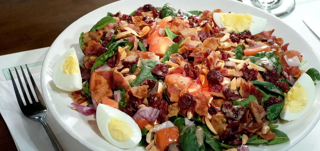 Spinach salad with bacon, cranberries, almonds, egg, and tomatoes.