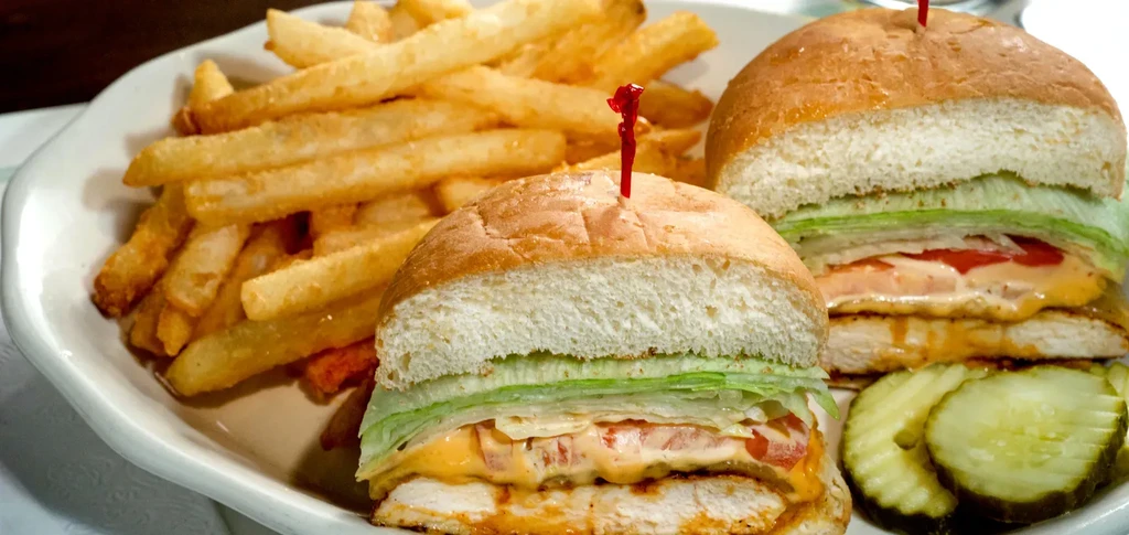Two chicken sandwiches, fries, and pickles on a white plate.