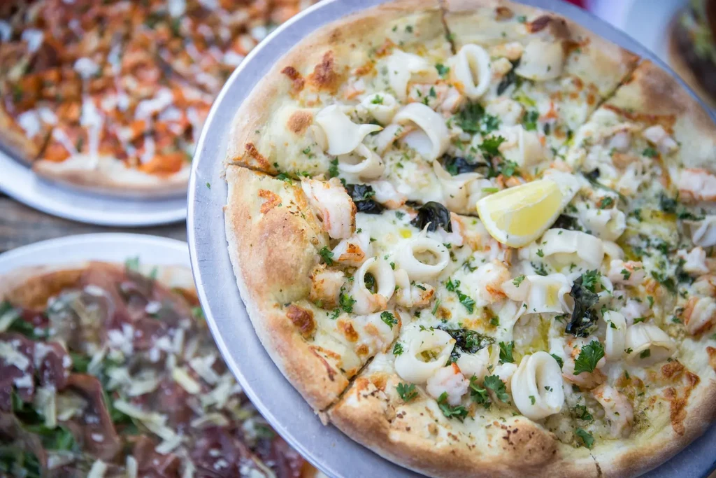 Close-up of a shrimp and calamari pizza with a lemon slice.