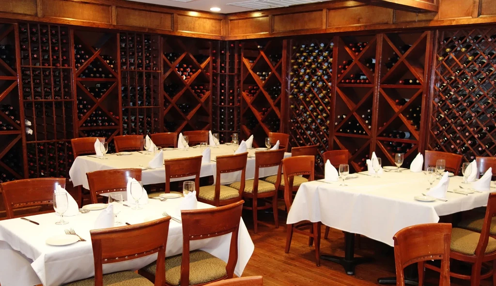 Upscale dining room with set tables and extensive wall-lined wine racks.