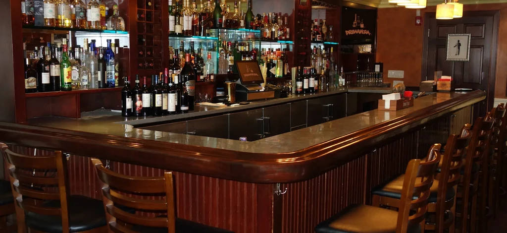 L-shaped dark wooden bar, well-stocked with backlit liquor bottles.