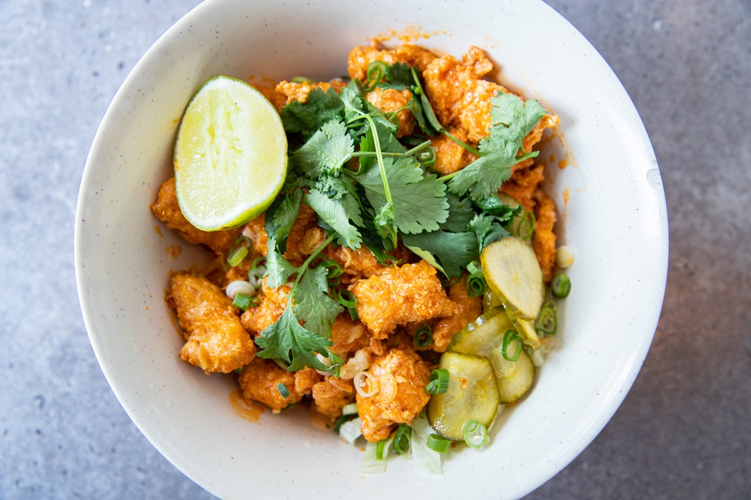 Fried bites with lime, cilantro, green onions, and pickled cucumbers.