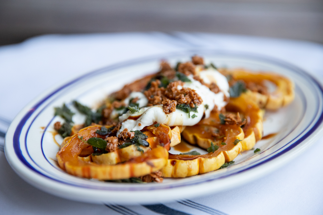 Sliced squash with creamy white topping, brown crumbles, and green leaves.