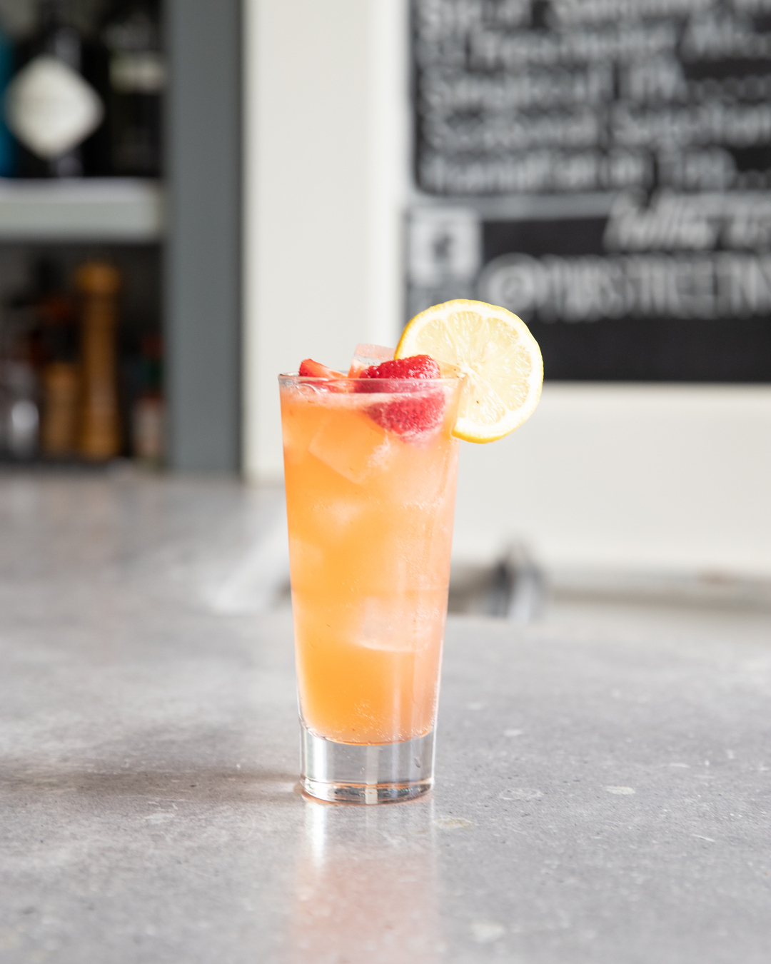 Tall glass of iced strawberry lemonade with strawberries and lemon.