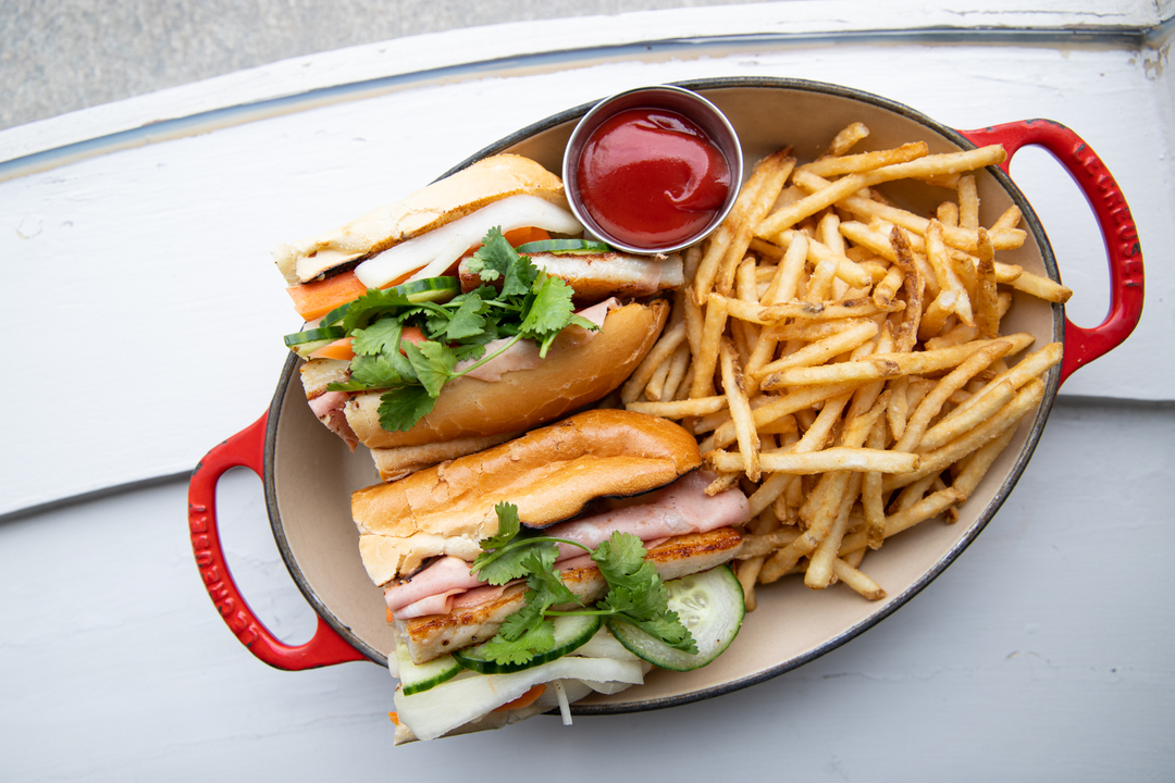 Banh mi sandwiches, french fries, and ketchup in a red skillet.