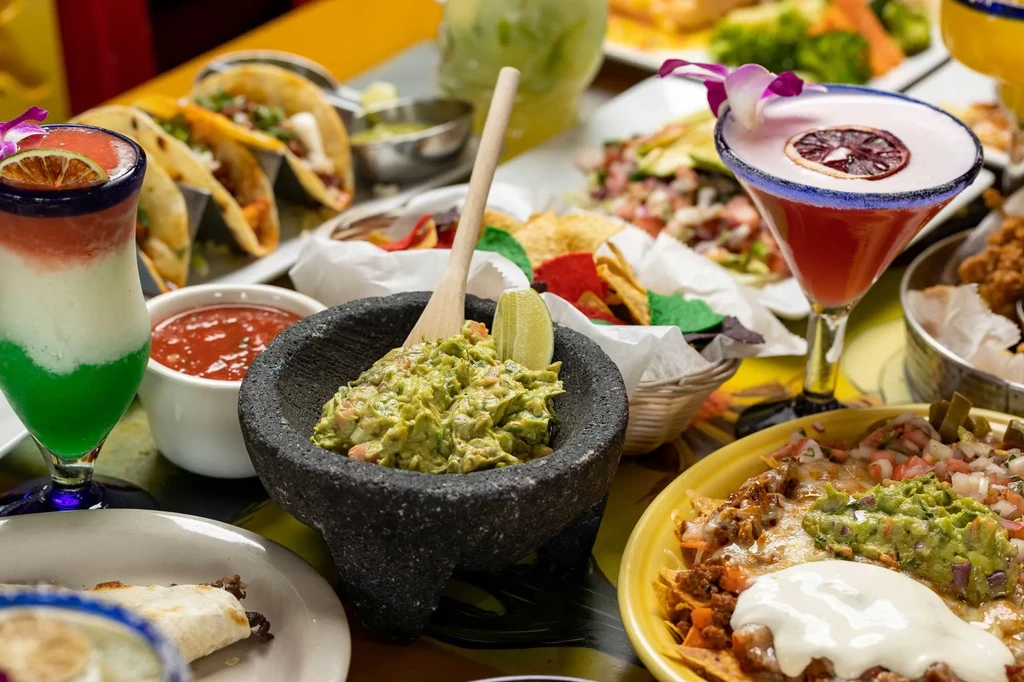 Vibrant Mexican food spread: guacamole, nachos, tacos, salsa, and colorful cocktails.