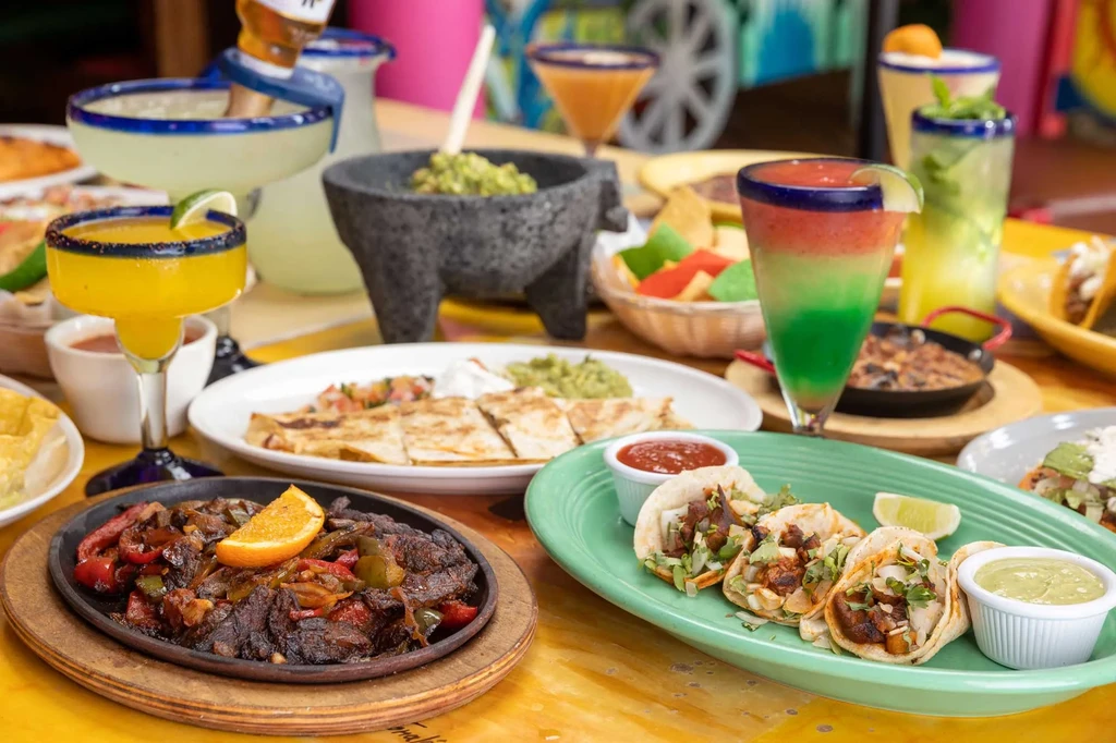 Vibrant Mexican food spread with fajitas, tacos, guacamole, chips, and margaritas.
