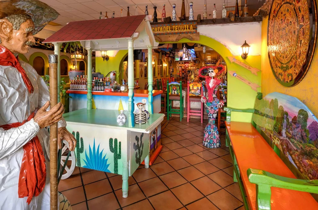 Colorful Mexican restaurant interior with statues and 'CATA DEL TEQUILA' bar.