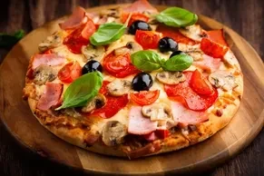 A whole pizza with ham, mushrooms, tomatoes, olives, and basil leaves.