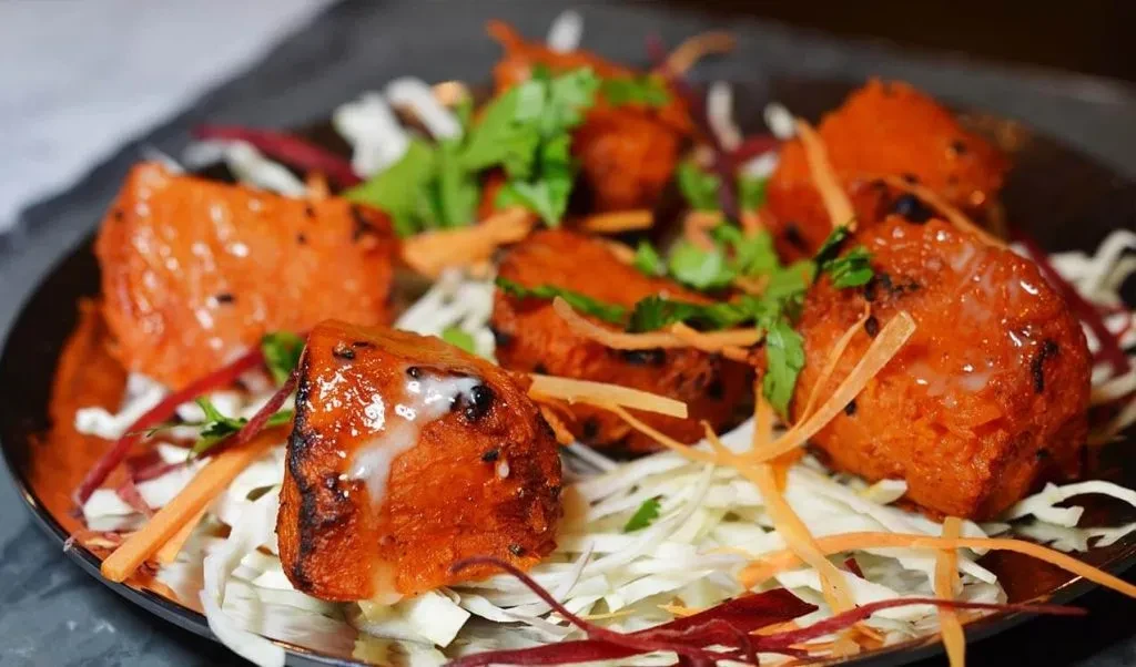 Orange glazed chunks of food with white sauce, cilantro, and shredded vegetables.