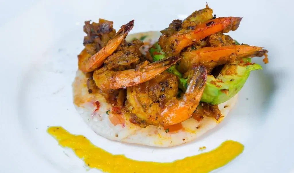 Spiced shrimp and avocado on a flatbread with a yellow sauce.