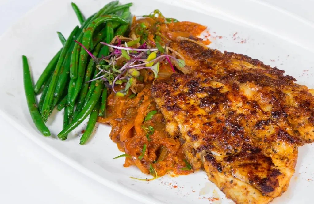 Grilled fish with green beans and a side of stewed vegetables.