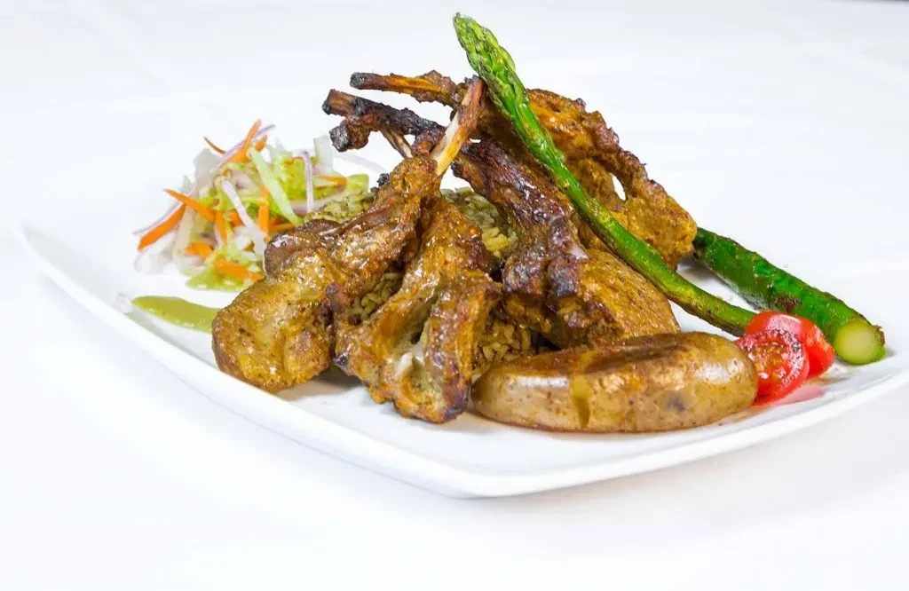 Lamb chops with asparagus, potatoes, and salad on a white plate.