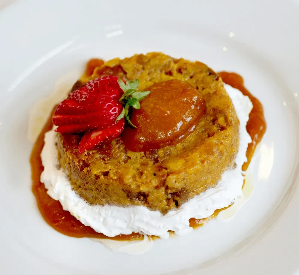 Dessert on a white plate with strawberries, cream, and apricot jam.