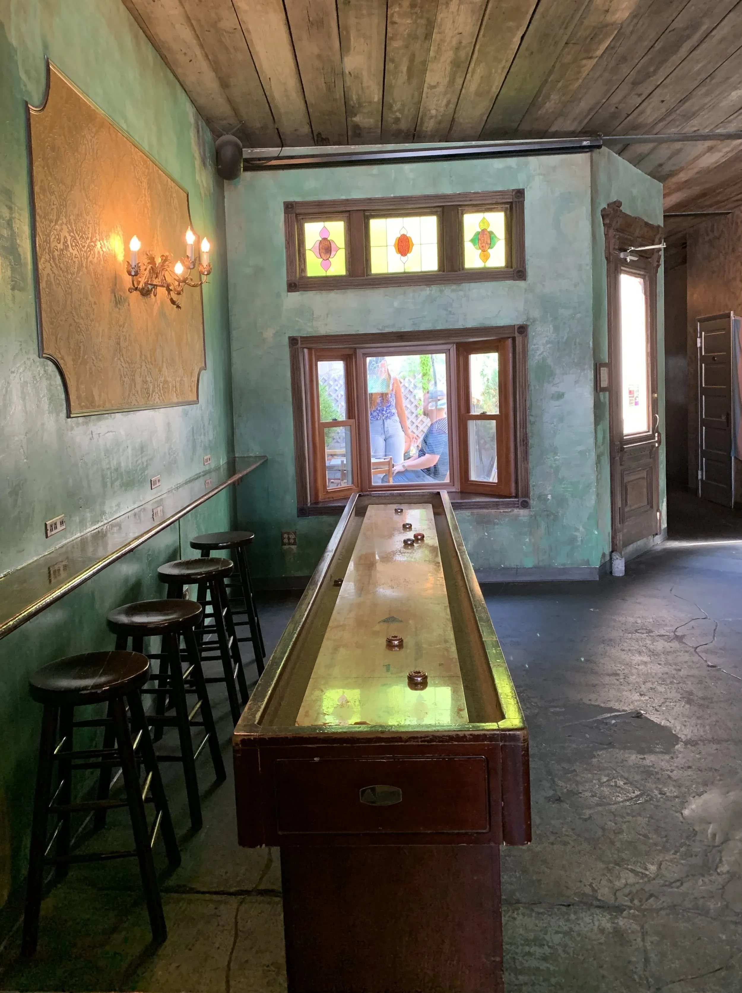 A vintage shuffleboard table in a room with stained glass windows.