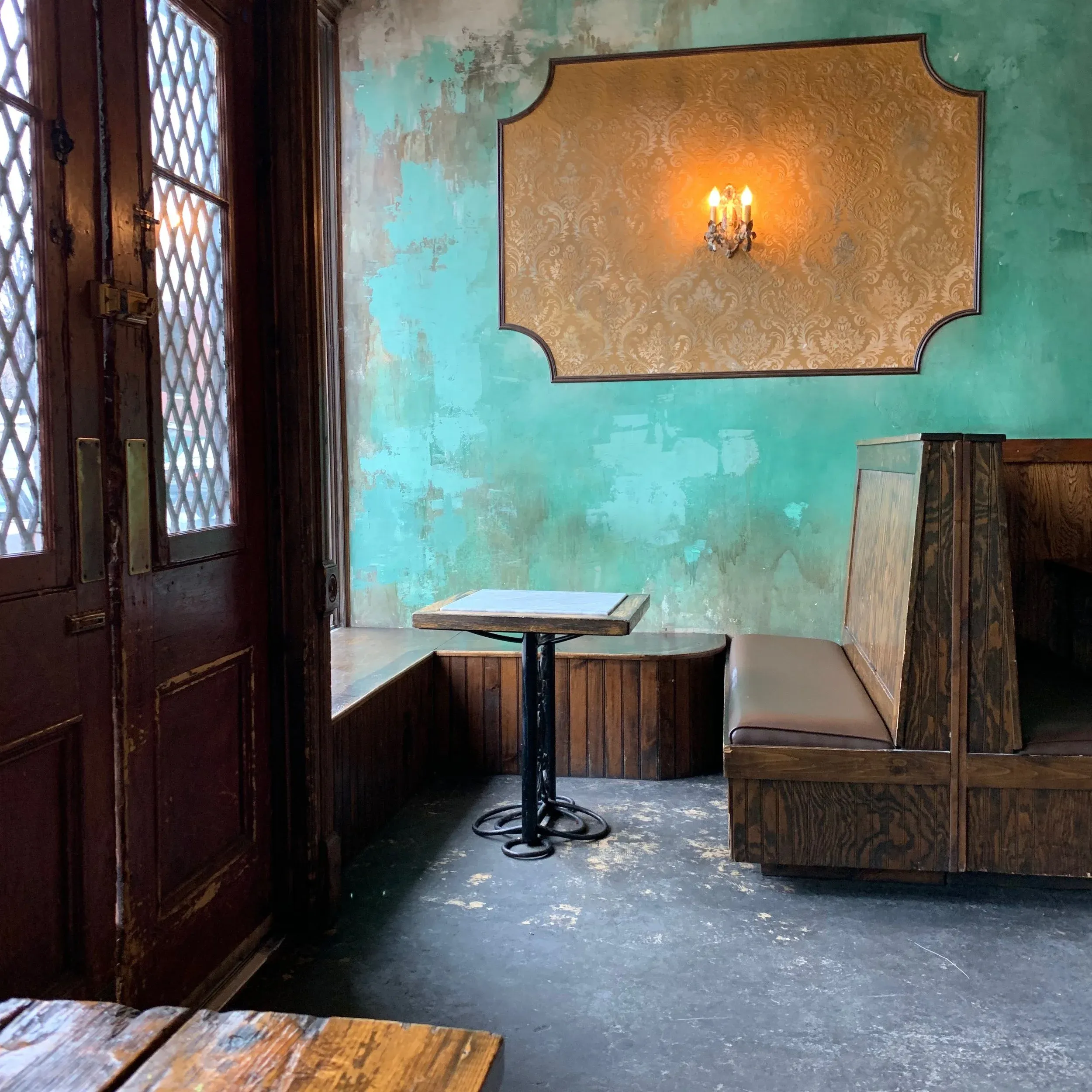Restaurant interior with peeling turquoise walls, wooden booths, and a decorative sconce.