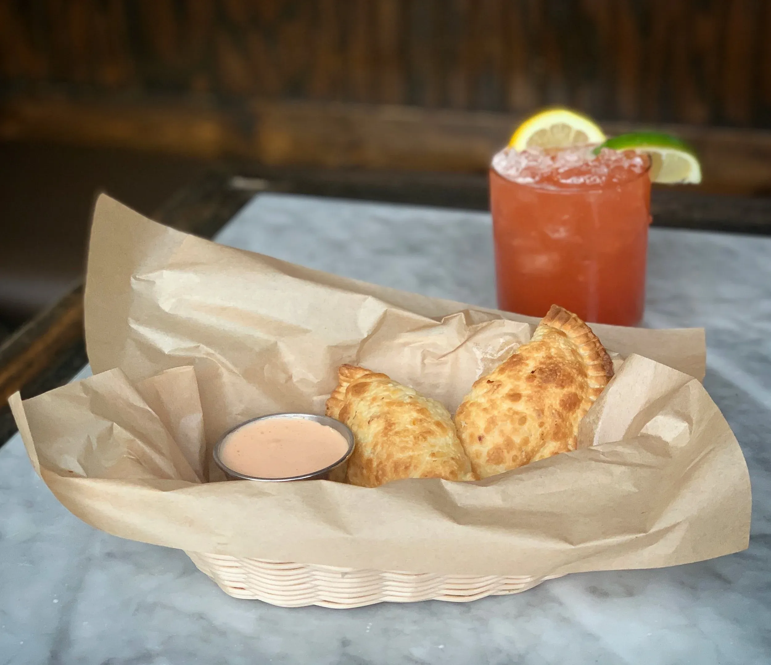 Two golden-brown pastries, sauce, and a garnished red cocktail.