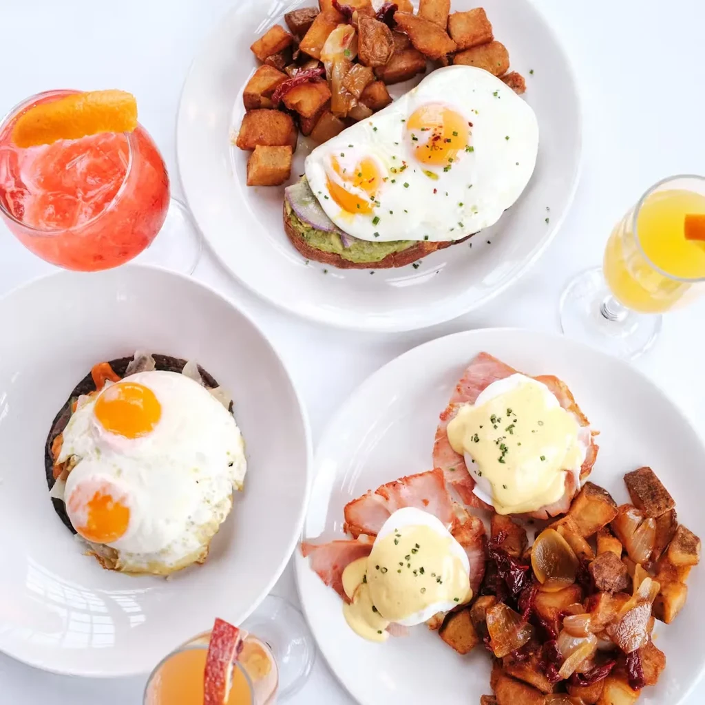 Overhead view of three brunch plates and two drinks on a white table.