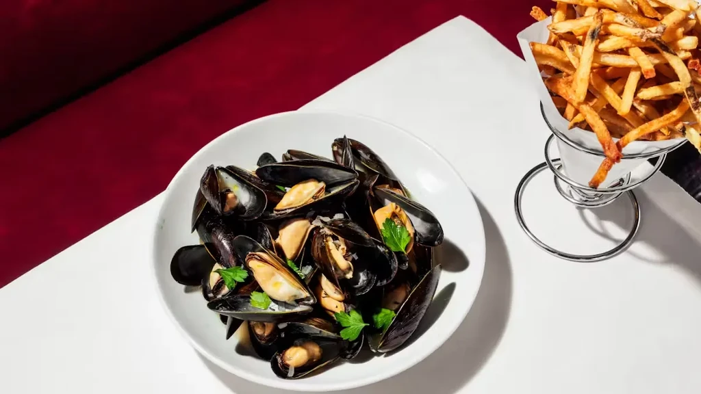 A plate of mussels with parsley and a side of french fries.