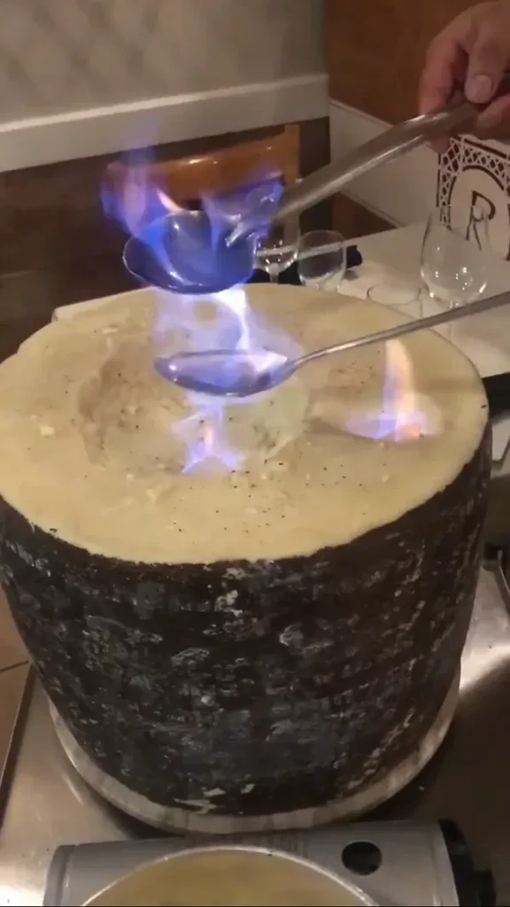 Flaming alcohol is poured into a wheel of melting cheese.