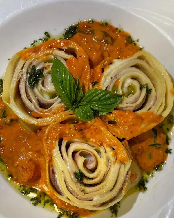 Pasta rolls with red sauce, green oil, and a basil leaf.