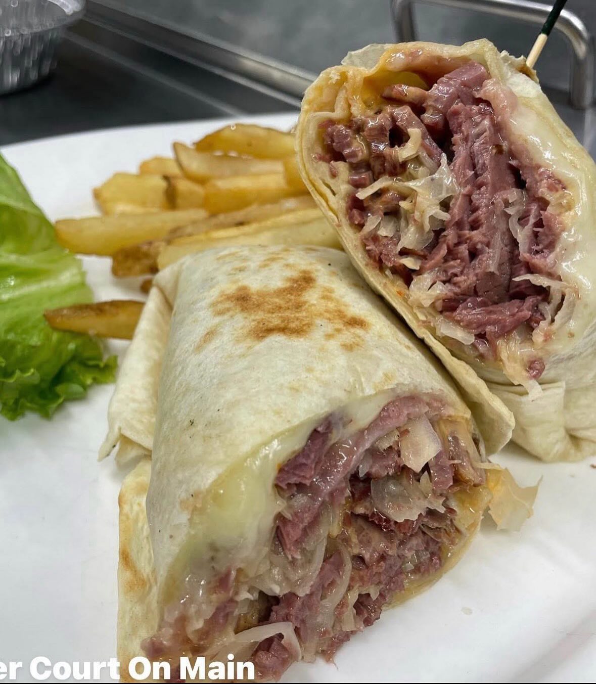 Two corned beef and cheese wraps, with fries and lettuce.