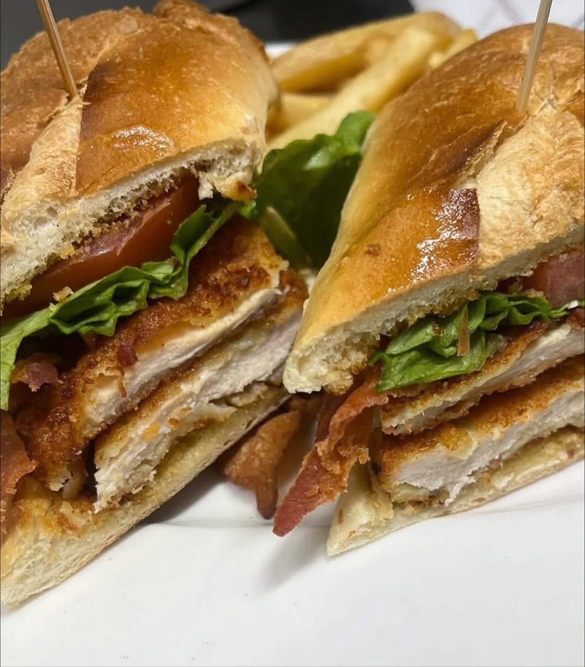 Crispy chicken sandwich halves with lettuce, tomato, bacon, and fries.