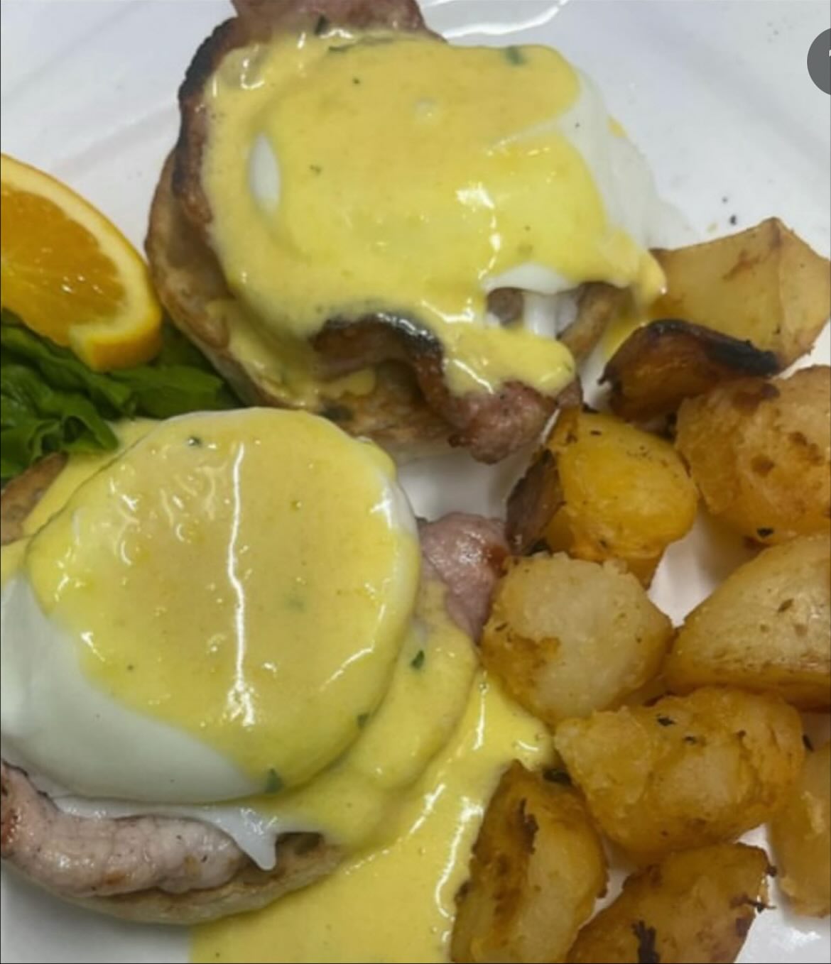 Eggs Benedict with hollandaise sauce, roasted potatoes, orange, and lettuce.