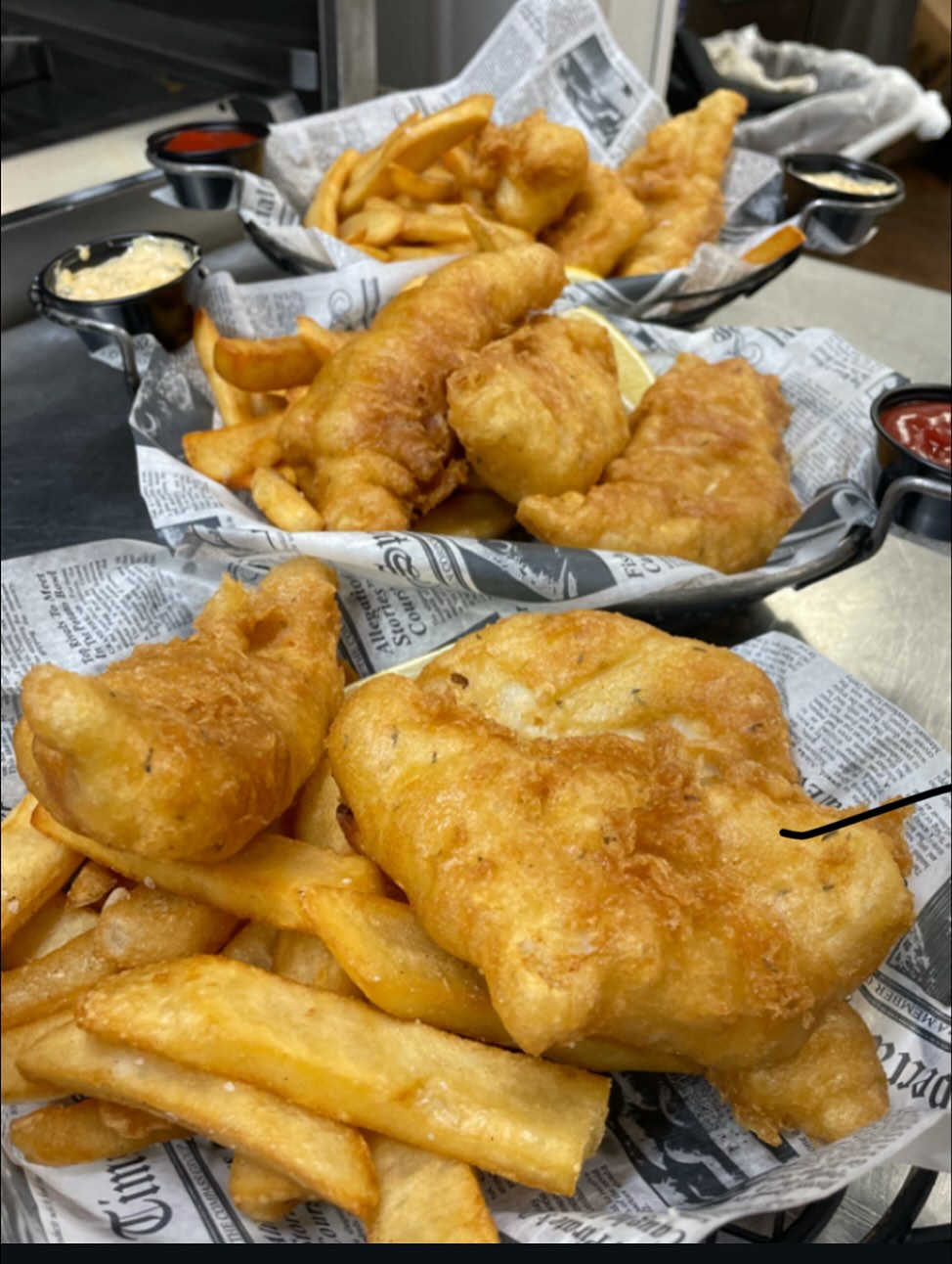Three baskets of crispy fish and chips with sauces.