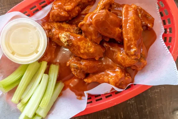 Buffalo chicken wings in a red basket with celery and dipping sauce.