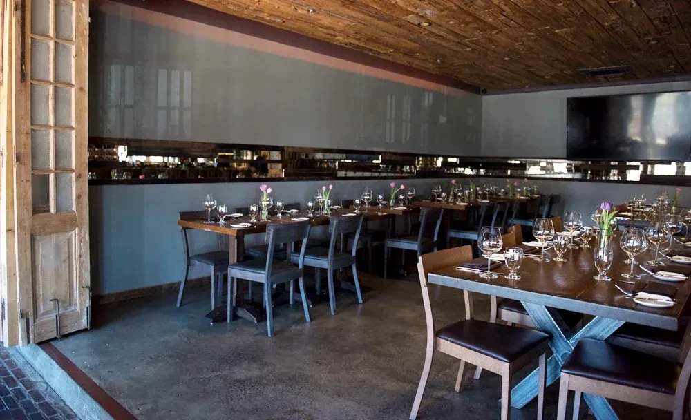 Restaurant dining room with set tables, wood ceiling, and an open doorway.