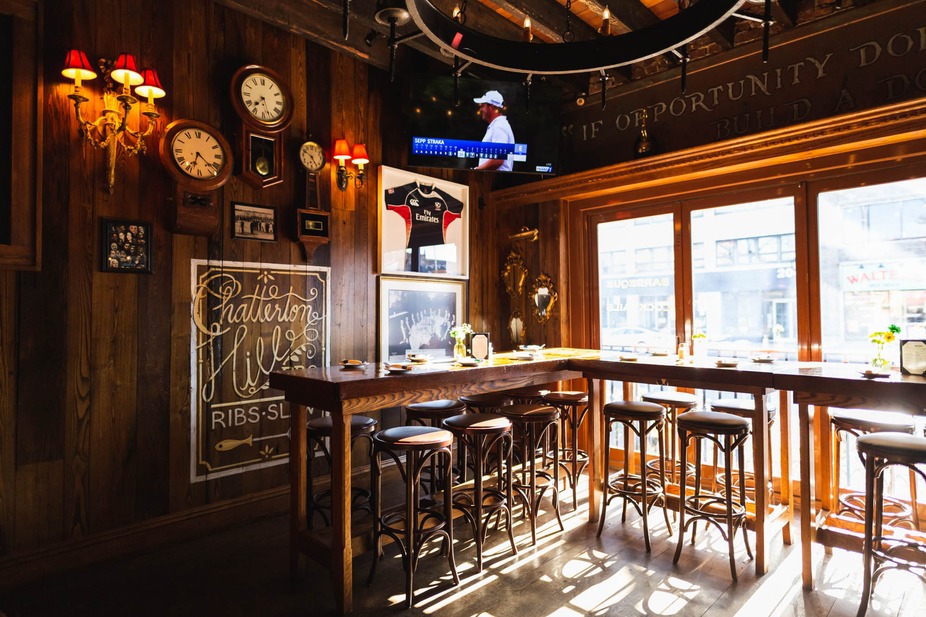 Restaurant interior with wooden walls, high tables, and sunlit windows.