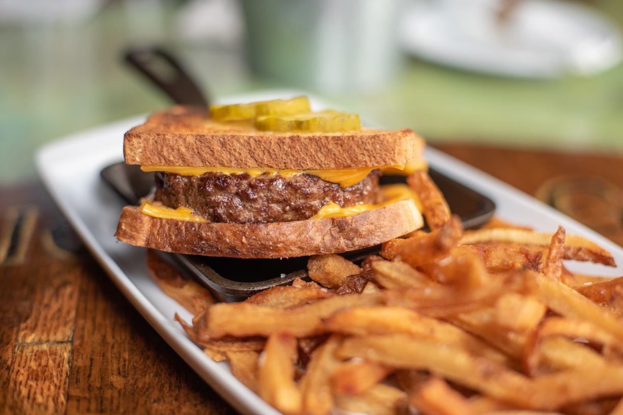 Patty melt sandwich with cheese, pickles, and fries on a white plate.