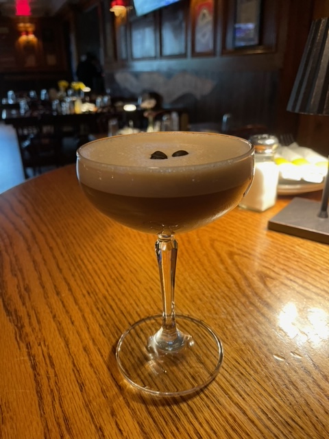 Martini glass with foamy drink and two coffee beans on wooden table.