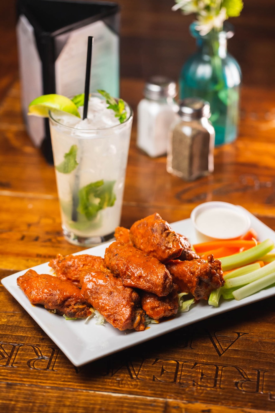 Plate of sauced chicken wings, celery, carrots, dipping sauce, and a cocktail.