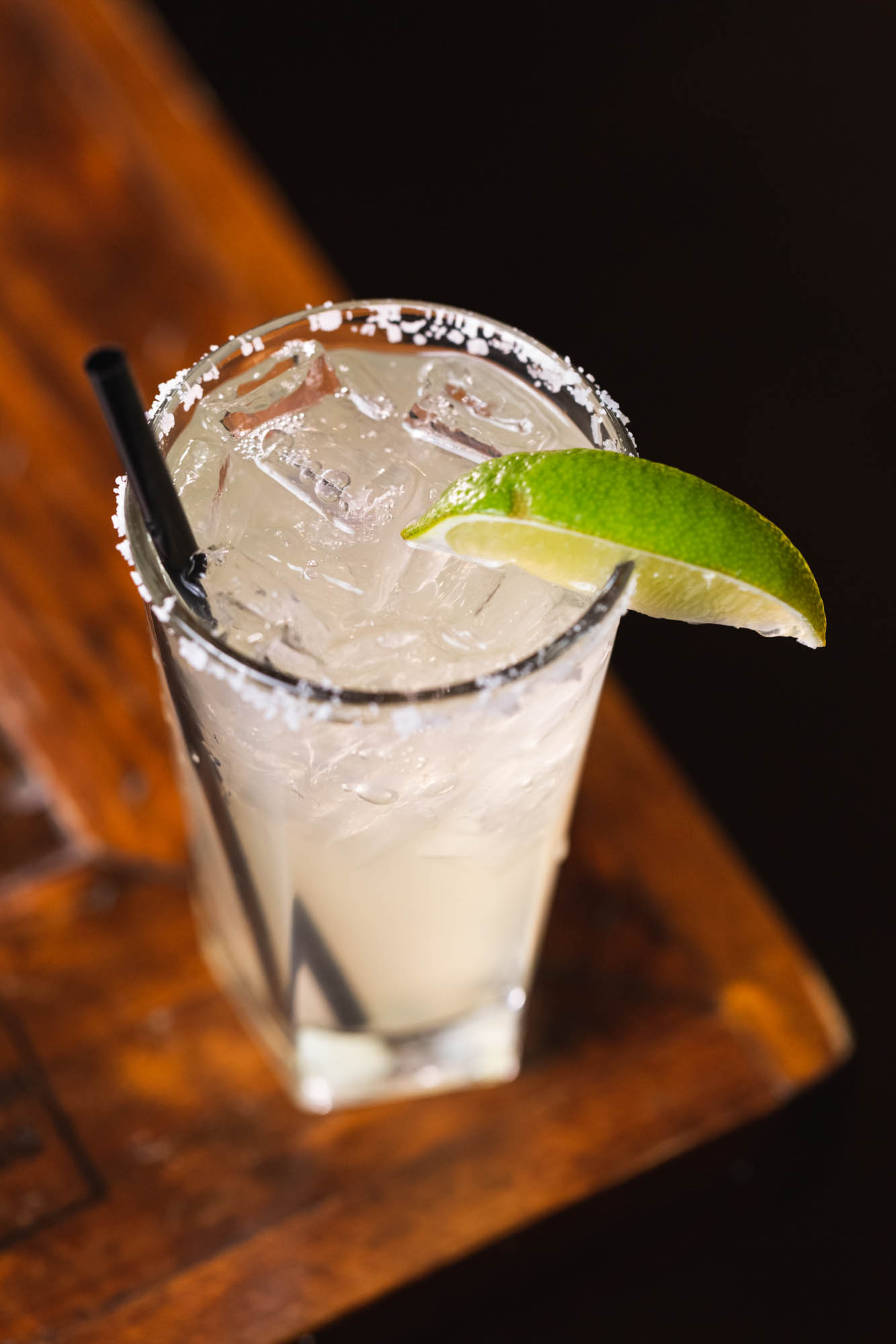 Glass with light drink, ice, salted rim, lime wedge, and straw.