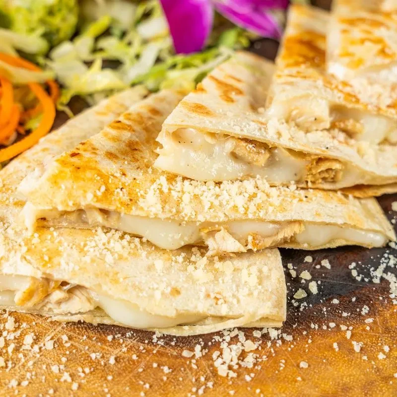 A stack of chicken and cheese quesadilla triangles on a wooden board.