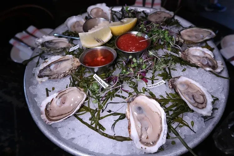 A dozen oysters, lemon wedges, and two sauces on a bed of ice.