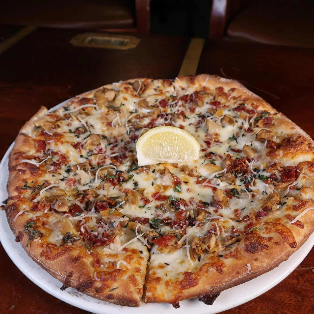 Pizza topped with white sauce, mushrooms, bacon, and herbs.