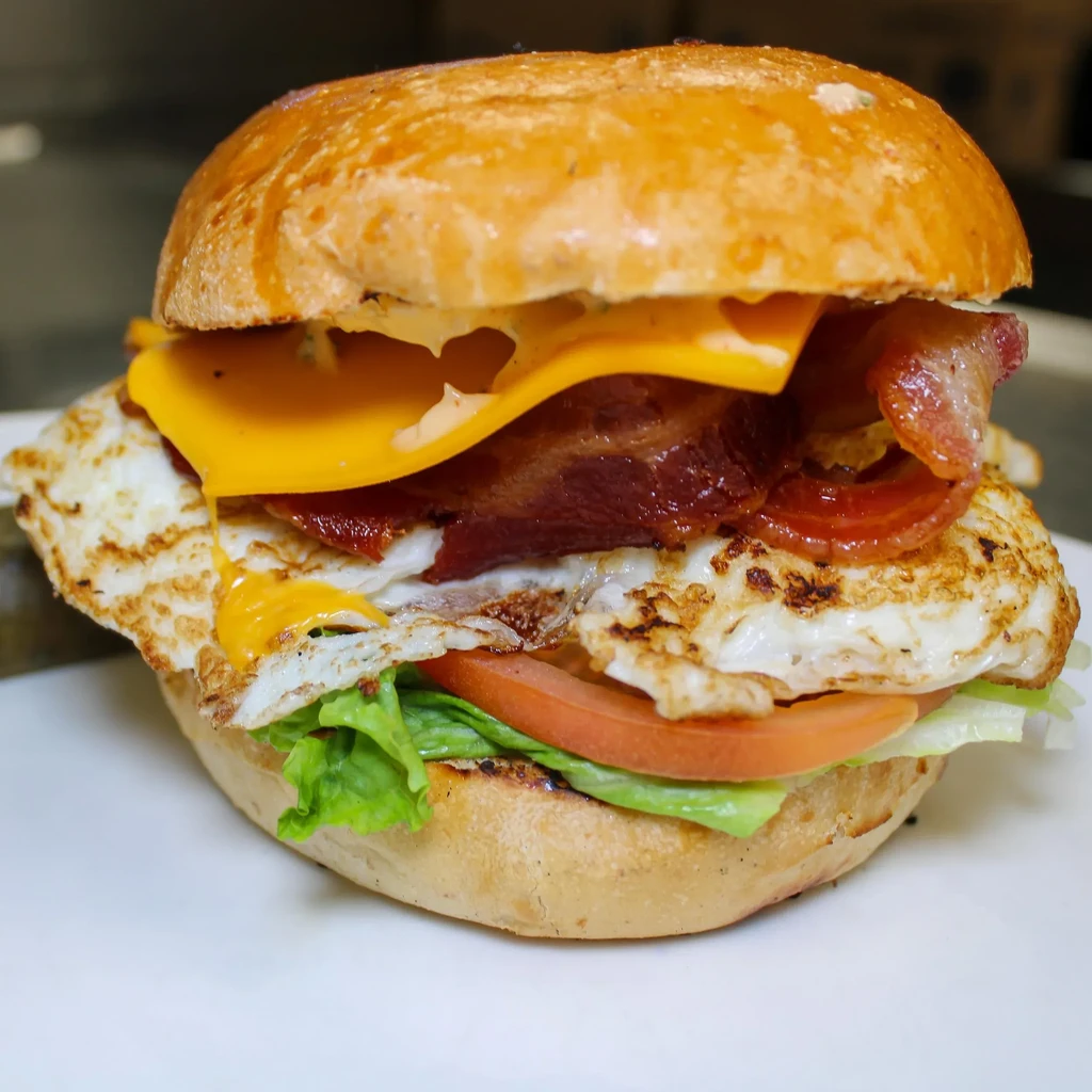 A breakfast sandwich with bacon, egg, cheese, lettuce, and tomato.