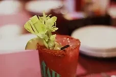 Red drink with celery and lime garnish, plates in background.