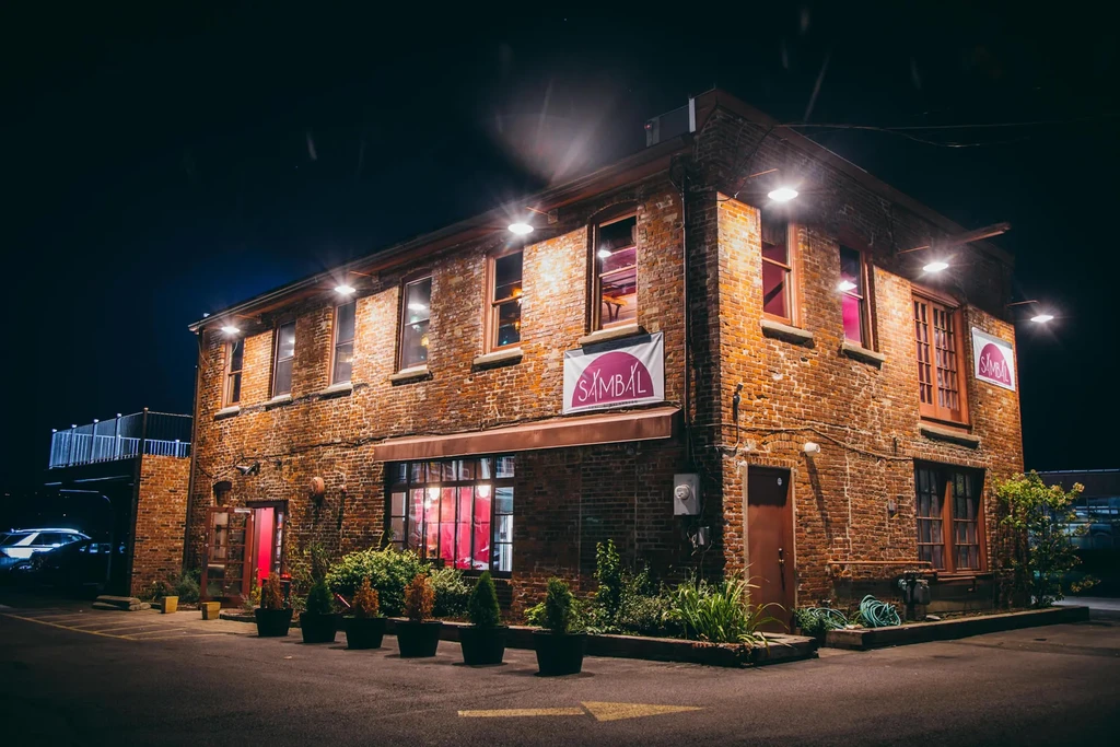 A brick building with "SAMBAL" signs glows under lights at night.