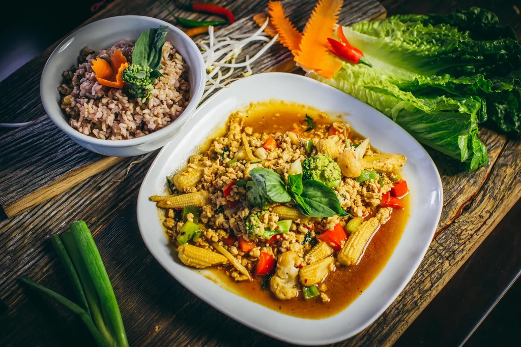 A plate of Thai food with rice, stir-fry, and fresh vegetables.