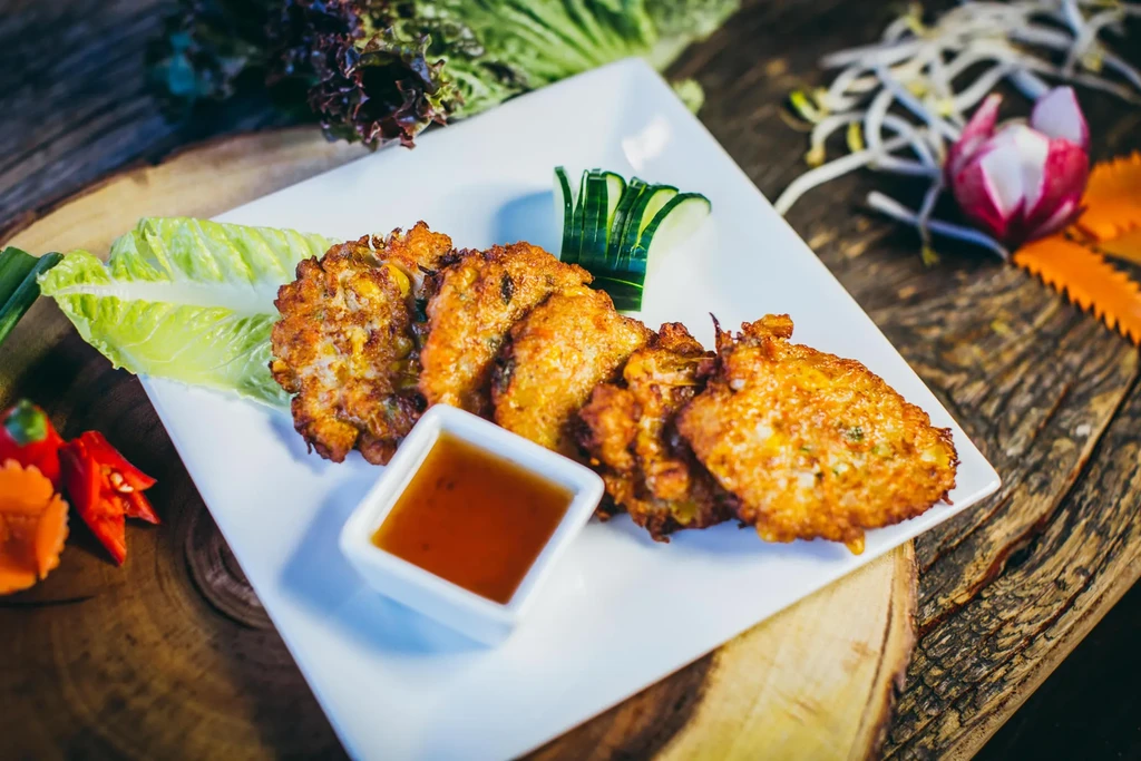Six golden brown corn fritters with sauce, cucumber, and lettuce.