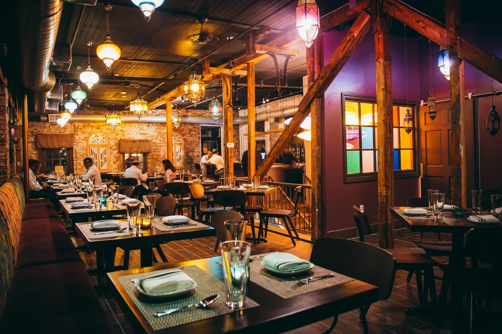 A restaurant with amber lighting, exposed brick, and customers dining at tables.