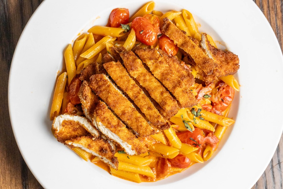 Penne pasta with sliced fried chicken, cherry tomatoes, and basil.