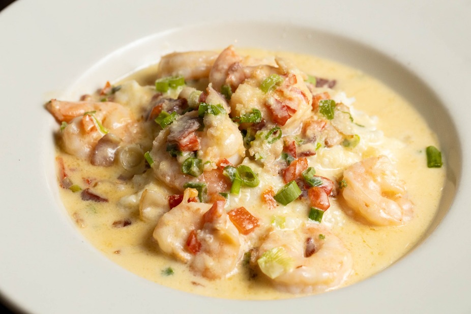 Shrimp and grits in a creamy sauce, garnished with tomatoes and green onions.