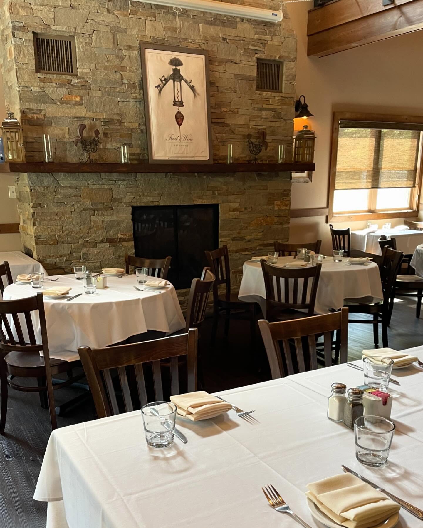 Restaurant dining room with set tables and a large stone fireplace.